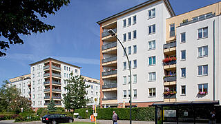 Straßenseitige Aufnahme der Gebäude Falkenberger Straße 160 - 163 und Wittlicher Straße 2 - 4. Zwei sechsstöckige Eckhäuser mit keilförmigen, innenliegenden Balkonen und ein fünfgeschossiges angrenzendes Gebäude auf der rechten Seite. Links im Hintergrund ein weiteres identisches Gebäude.