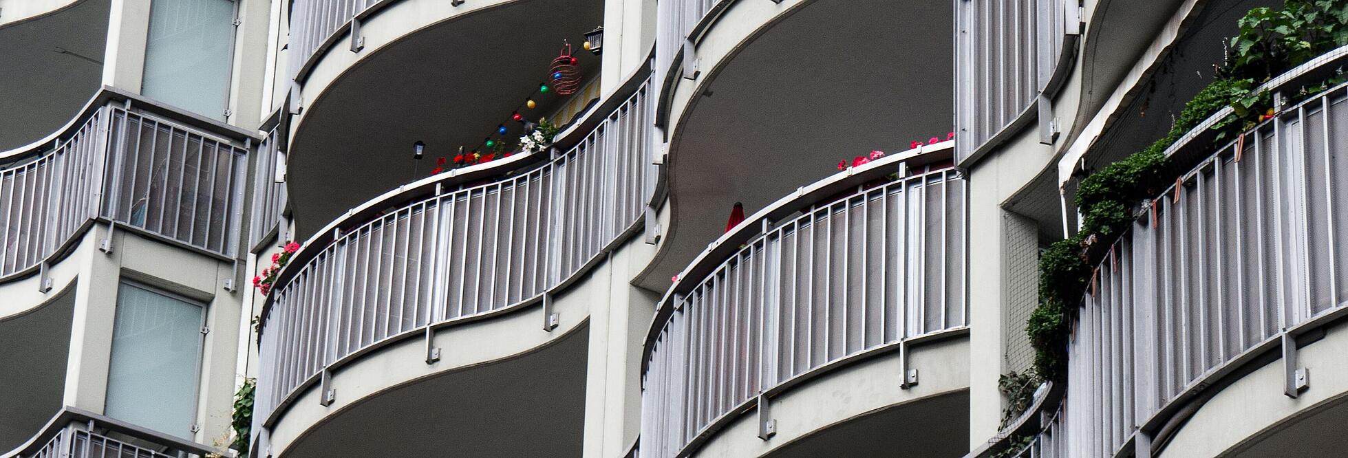 Aufnahem von unten: Eine Fassade mit wellenförmigen Balkonen und ebenfalls wellenförmigen Balustraden aus Metallstreben.