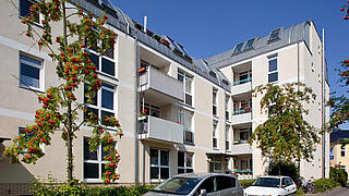 Außenaufnahme der Fassade des Hauses Blankenburger Weg 2 - 4d, sichtbar die bewachsene Fassade und zwei Balkone sowie Teil des Quergebäudes. Im Vordergrund parken Autos auf der Straße.